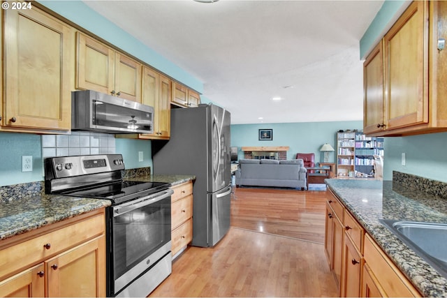 kitchen featuring appliances with stainless steel finishes, sink, light hardwood / wood-style flooring, and dark stone countertops