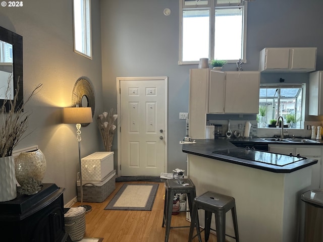 kitchen with sink, white cabinetry, kitchen peninsula, light hardwood / wood-style floors, and a high ceiling