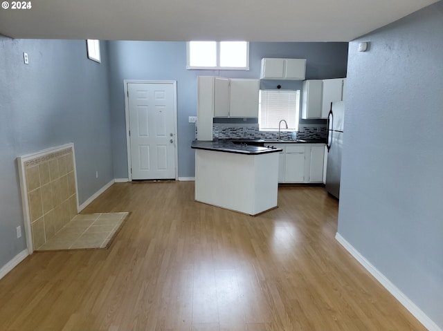 kitchen with sink, light wood-type flooring, stainless steel fridge, decorative backsplash, and white cabinets