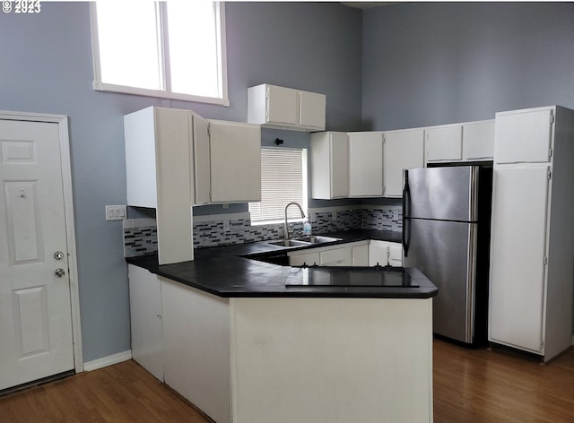 kitchen featuring stainless steel refrigerator, sink, backsplash, white cabinets, and kitchen peninsula