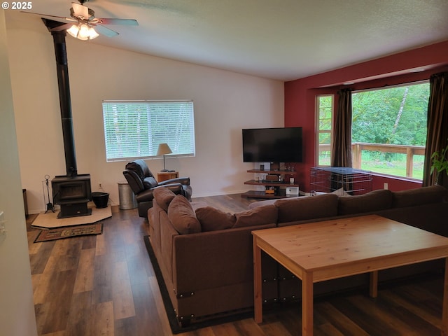 living room featuring a wood stove, wood finished floors, ceiling fan, and vaulted ceiling