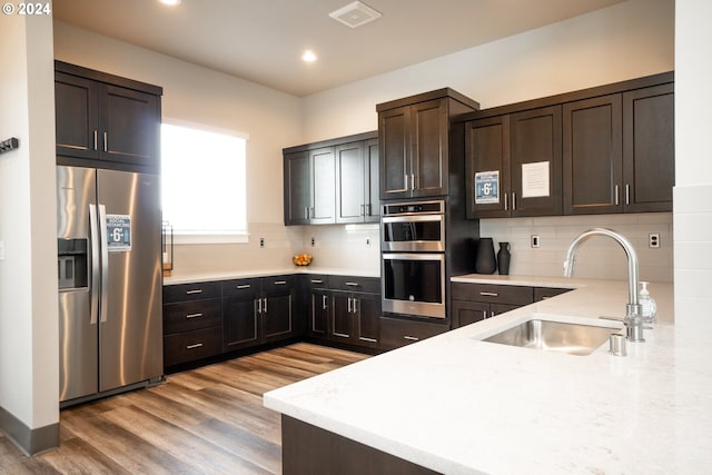 kitchen with tasteful backsplash, dark brown cabinets, stainless steel appliances, sink, and light hardwood / wood-style floors