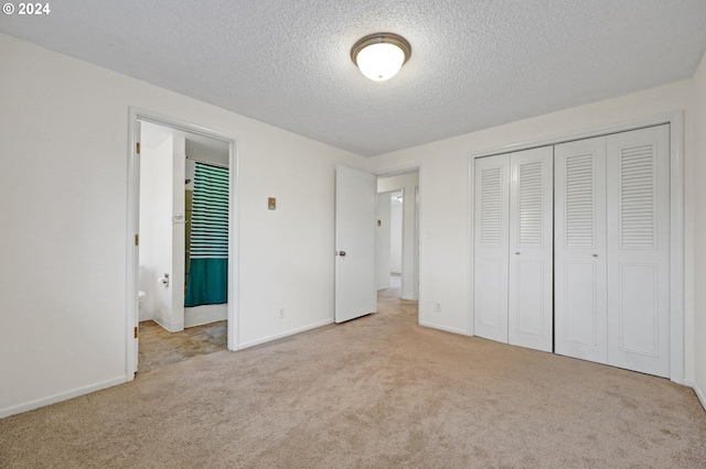 unfurnished bedroom featuring ensuite bath, light carpet, a textured ceiling, and a closet