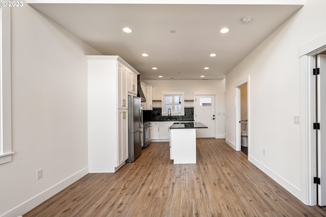 kitchen with backsplash, white cabinets, stainless steel fridge, light wood-type flooring, and a kitchen island