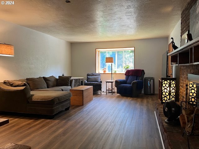46791 Winfrey Rd, Westfir, OR 97492 - living room with dark wood-style floors, a textured ceiling, and a brick fireplace
