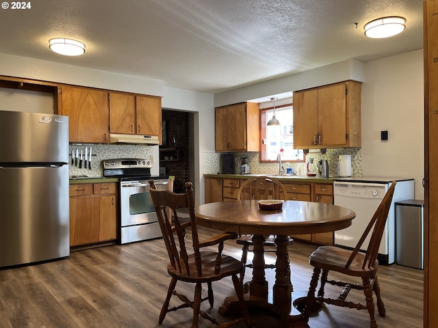 46791 Winfrey Rd, Westfir, OR 97492 - kitchen with appliances with stainless steel finishes, a textured ceiling, under cabinet range hood, brown cabinets, and tasteful backsplash