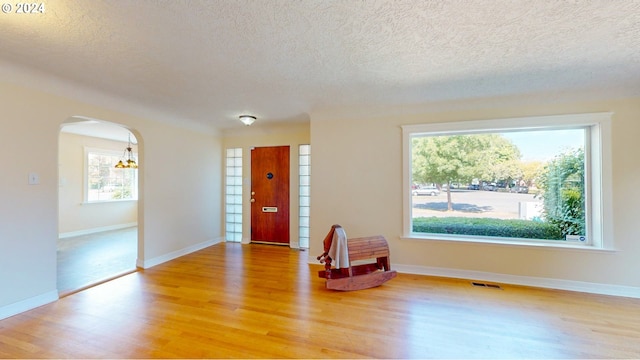 entryway with a textured ceiling, wood-type flooring, and a chandelier