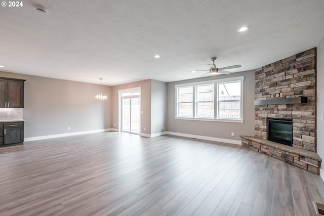 unfurnished living room with a fireplace, light hardwood / wood-style floors, ceiling fan with notable chandelier, and a textured ceiling