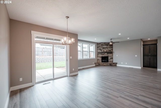 unfurnished living room featuring a stone fireplace, hardwood / wood-style floors, ceiling fan with notable chandelier, and a textured ceiling