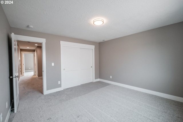 unfurnished bedroom featuring a closet, a textured ceiling, and light carpet