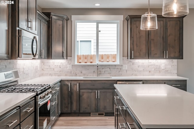 kitchen featuring light hardwood / wood-style floors, stainless steel appliances, hanging light fixtures, sink, and tasteful backsplash