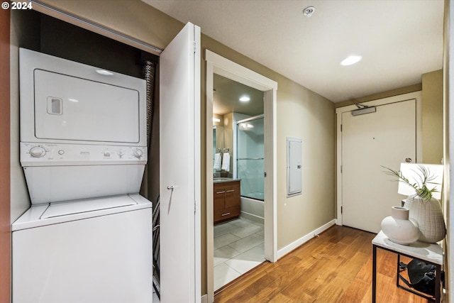 laundry room featuring light wood-type flooring, stacked washer / drying machine, and electric panel