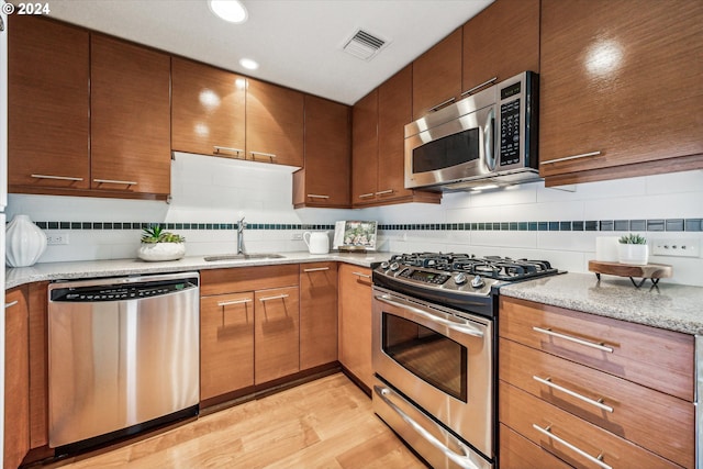 kitchen featuring decorative backsplash, light wood-type flooring, appliances with stainless steel finishes, and sink