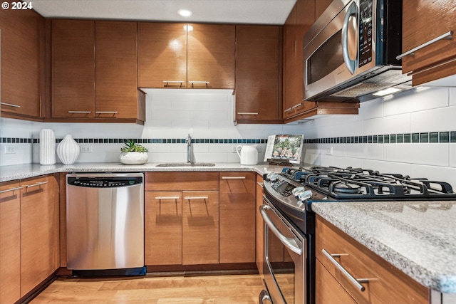 kitchen with light stone counters, appliances with stainless steel finishes, sink, and light hardwood / wood-style flooring