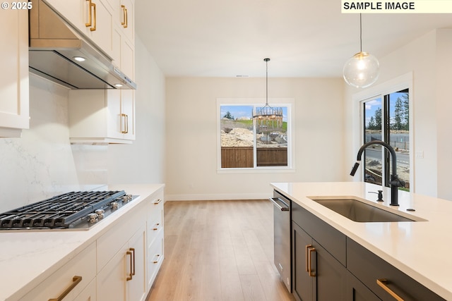 kitchen with a sink, appliances with stainless steel finishes, under cabinet range hood, decorative light fixtures, and tasteful backsplash