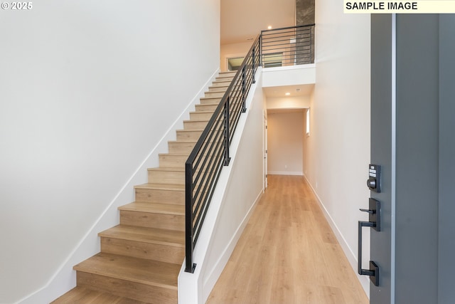 stairs featuring a high ceiling, wood finished floors, and baseboards