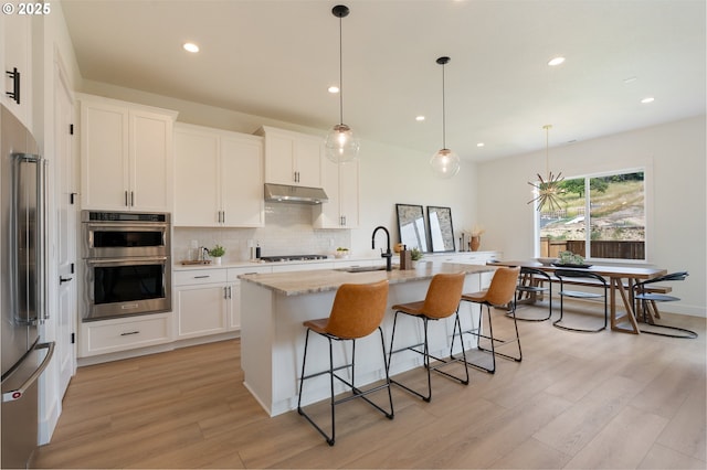 15044 SW 164th Ave Unit L17, Tigard, OR 97224 - kitchen with stainless steel appliances, under cabinet range hood, light wood finished floors, decorative backsplash, and a breakfast bar