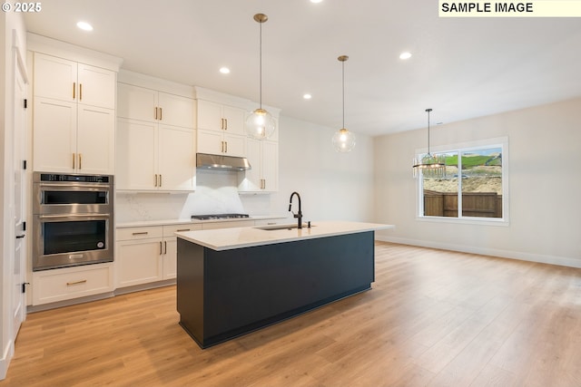 kitchen featuring under cabinet range hood, gas stovetop, stainless steel double oven, white cabinetry, and a sink