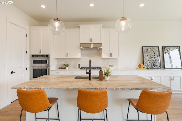 15044 SW 164th Ave Unit L17, Tigard, OR 97224 - kitchen featuring appliances with stainless steel finishes, decorative backsplash, under cabinet range hood, a kitchen bar, and light wood finished floors
