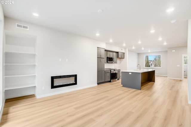 kitchen featuring sink, gray cabinets, stainless steel appliances, light hardwood / wood-style floors, and an island with sink