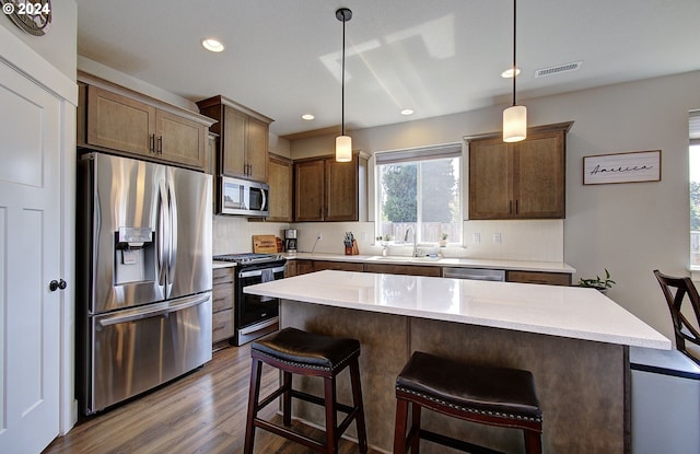 kitchen with dark wood-type flooring, stainless steel appliances, decorative light fixtures, and a kitchen island