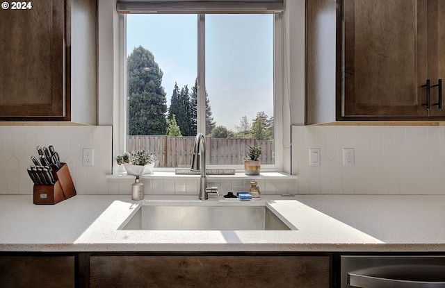 kitchen with dark brown cabinetry, plenty of natural light, light stone countertops, and sink