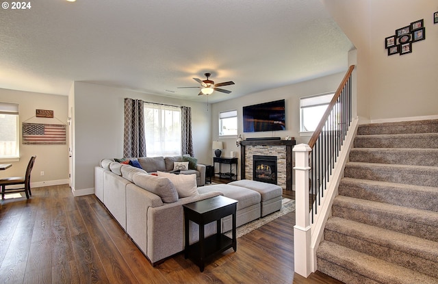 living room featuring a stone fireplace, dark wood-type flooring, a textured ceiling, and ceiling fan