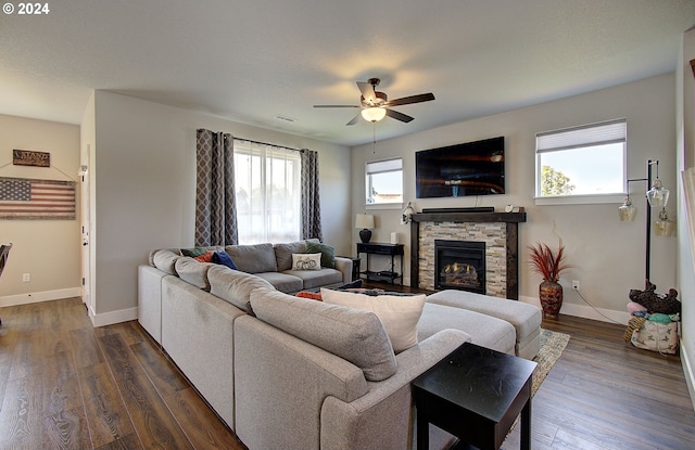 living room with dark hardwood / wood-style flooring, a stone fireplace, and ceiling fan