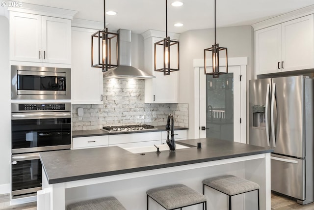 kitchen featuring white cabinetry, appliances with stainless steel finishes, pendant lighting, wall chimney range hood, and backsplash