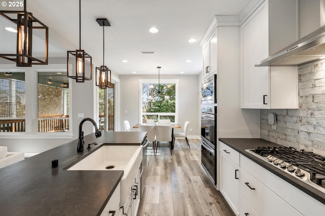 kitchen featuring decorative light fixtures, tasteful backsplash, white cabinetry, stainless steel appliances, and wall chimney range hood