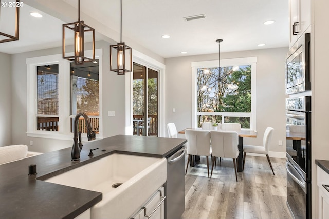 kitchen with hanging light fixtures, stainless steel appliances, white cabinets, and light wood-type flooring