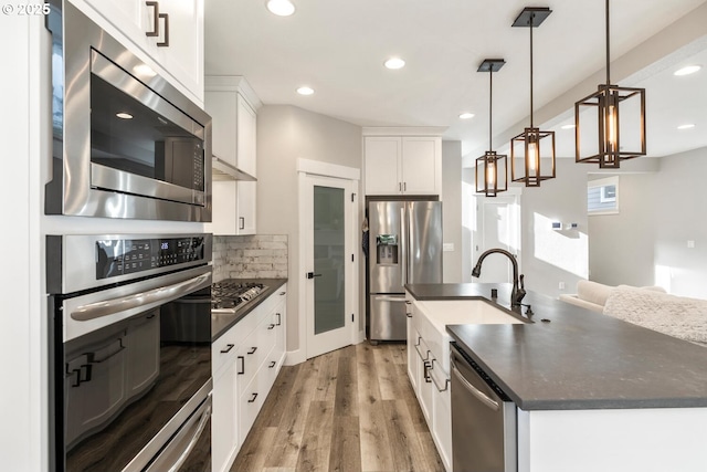 kitchen with sink, appliances with stainless steel finishes, decorative backsplash, white cabinets, and decorative light fixtures