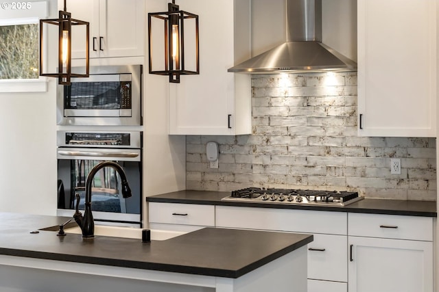 kitchen with wall chimney exhaust hood, pendant lighting, stainless steel appliances, decorative backsplash, and white cabinets