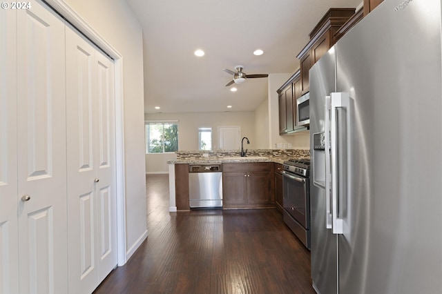 kitchen featuring ceiling fan, dark hardwood / wood-style floors, appliances with stainless steel finishes, light stone counters, and kitchen peninsula