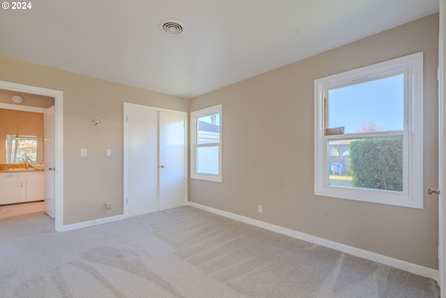 unfurnished bedroom featuring ensuite bath, light carpet, a closet, and sink