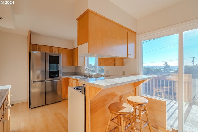 kitchen with sink, light wood-type flooring, kitchen peninsula, a breakfast bar area, and stainless steel refrigerator