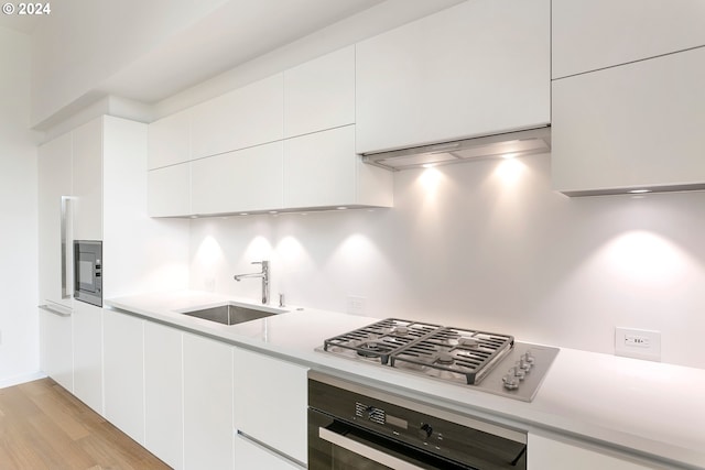 kitchen with white cabinets, stainless steel gas cooktop, sink, oven, and light hardwood / wood-style flooring