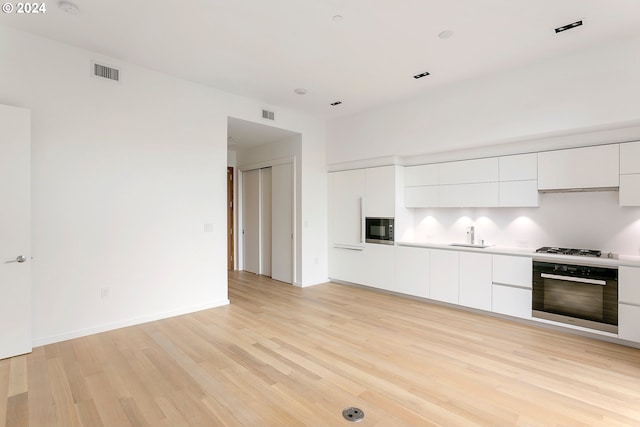 kitchen with white cabinets, stainless steel oven, black microwave, and light hardwood / wood-style flooring