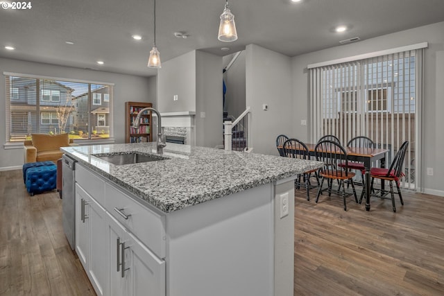 kitchen featuring a kitchen island with sink, hanging light fixtures, sink, white cabinetry, and wood-type flooring