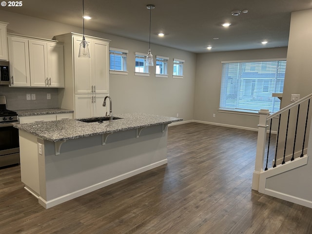 kitchen with light stone counters, a kitchen island with sink, stainless steel appliances, a sink, and hanging light fixtures