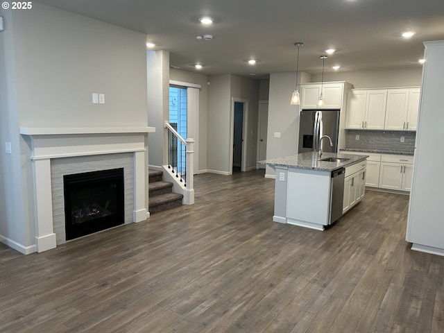 kitchen featuring white cabinets, an island with sink, appliances with stainless steel finishes, light stone counters, and hanging light fixtures