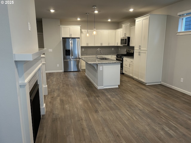 kitchen with a center island with sink, light stone counters, stainless steel appliances, pendant lighting, and a sink