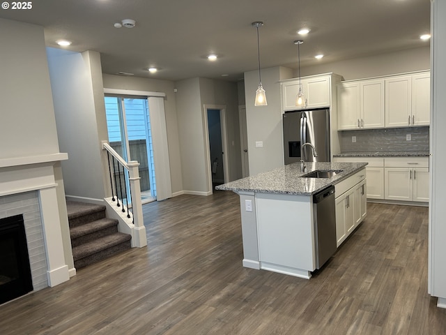 kitchen featuring white cabinets, an island with sink, appliances with stainless steel finishes, light stone countertops, and a sink