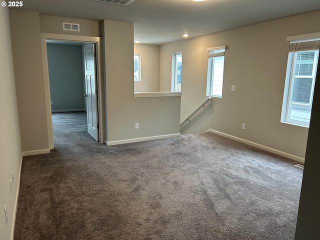 unfurnished room featuring dark colored carpet, a healthy amount of sunlight, and visible vents