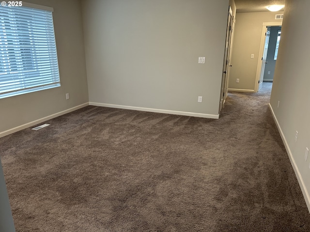 spare room with visible vents, dark carpet, and baseboards