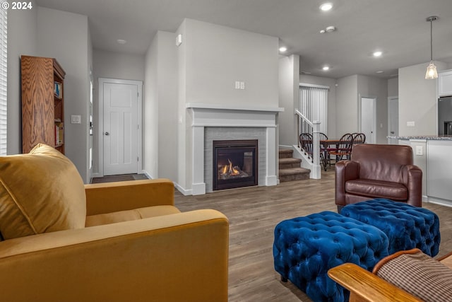 living area featuring baseboards, stairway, light wood-type flooring, a brick fireplace, and recessed lighting