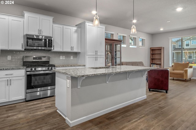 kitchen featuring hanging light fixtures, white cabinets, stainless steel appliances, and a center island with sink