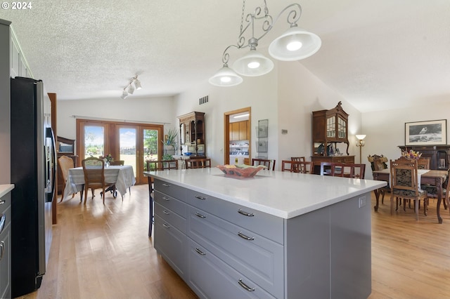 kitchen featuring gray cabinetry, stainless steel refrigerator with ice dispenser, decorative light fixtures, a kitchen island, and vaulted ceiling