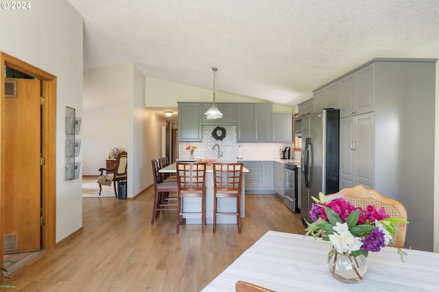 kitchen featuring light hardwood / wood-style floors, appliances with stainless steel finishes, decorative light fixtures, backsplash, and lofted ceiling