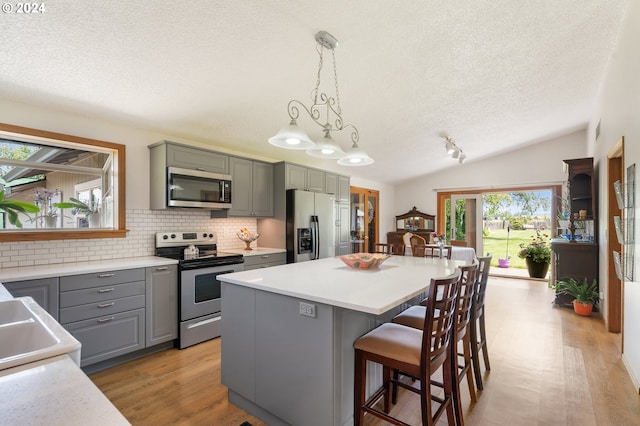 kitchen featuring a kitchen island, stainless steel appliances, backsplash, hanging light fixtures, and vaulted ceiling